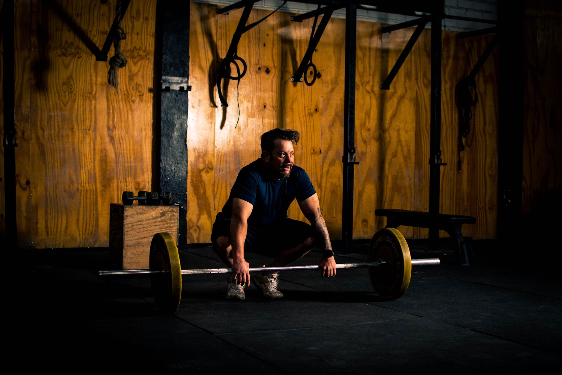 A lifter crouches over a loaded barbell to set his grip in a dimly lit gym