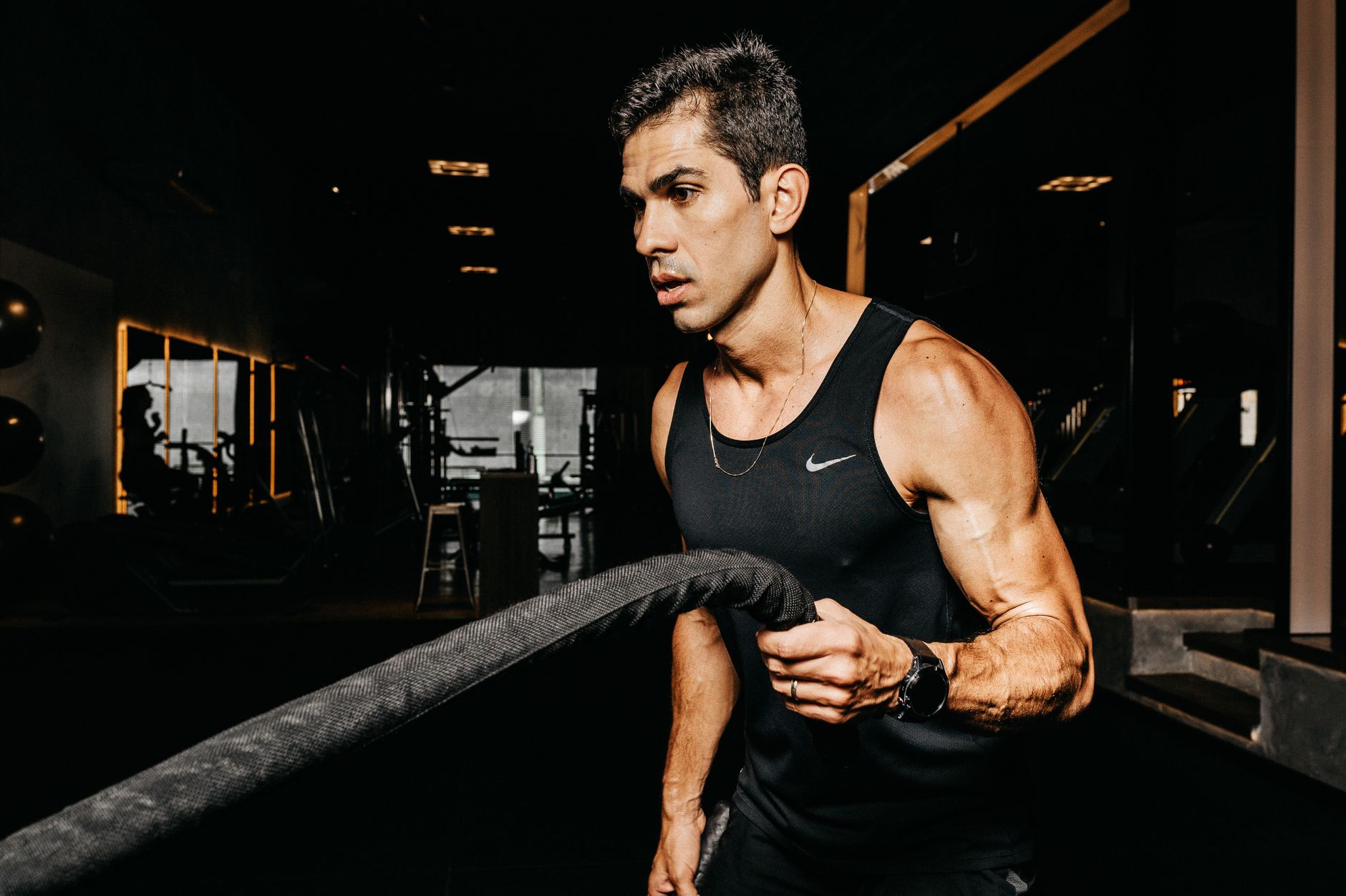 A man works battle ropes mid-set in a dark gym lit by a warm glow