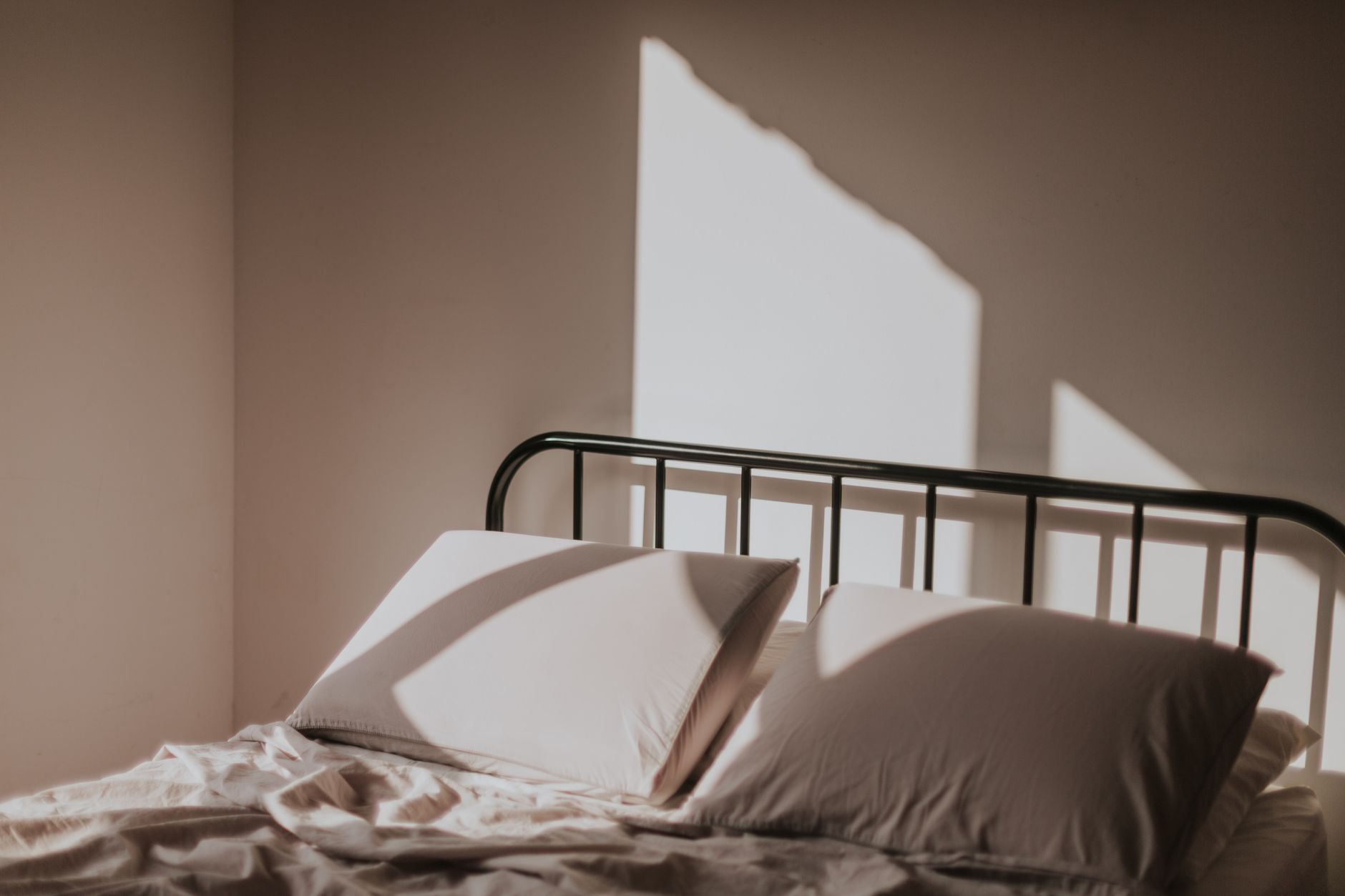 Morning light casting sharp shapes above a bed with an iron bedhead and soft linen
