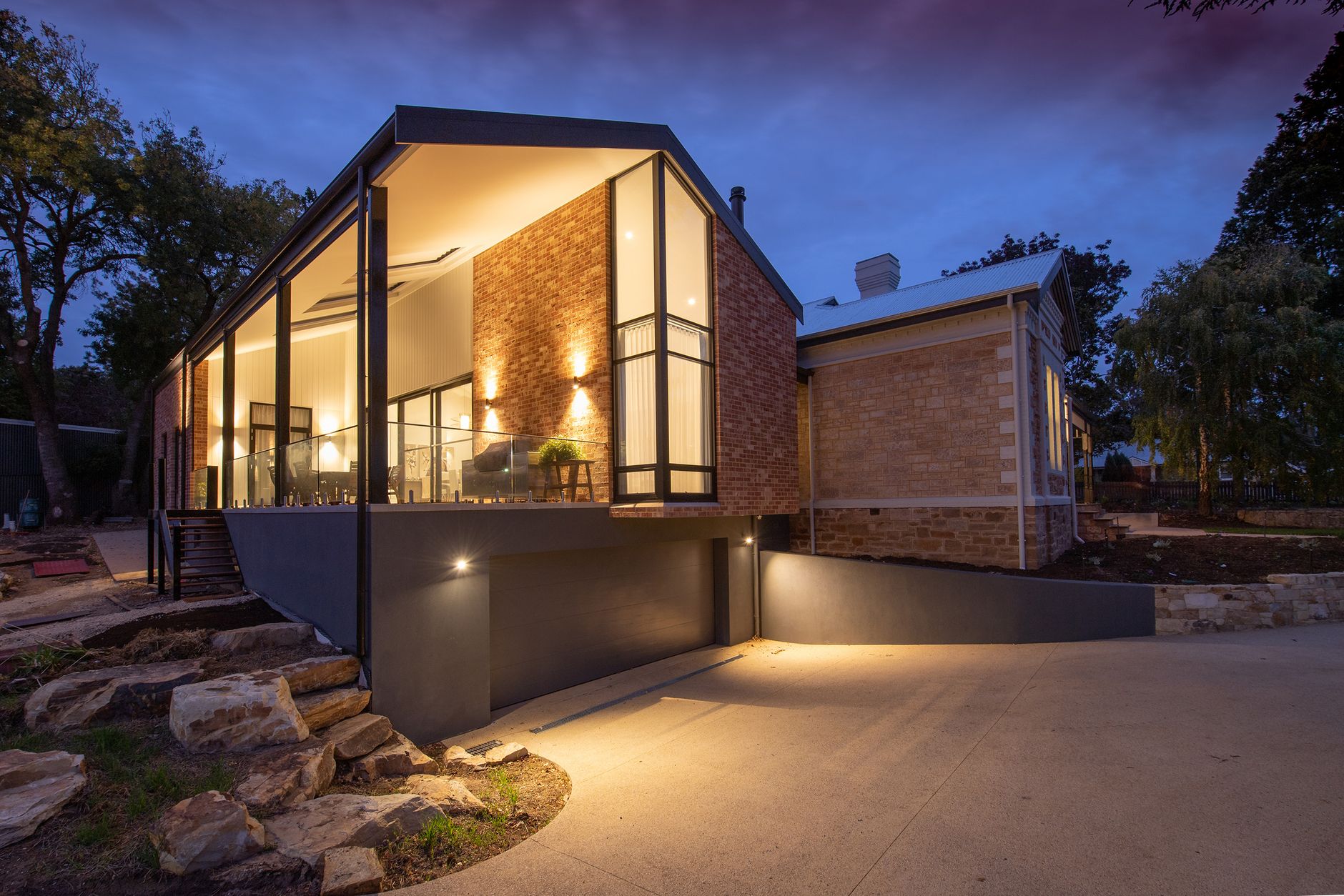 A renovated brick and glass extension glowing at dusk beside a heritage stone villa