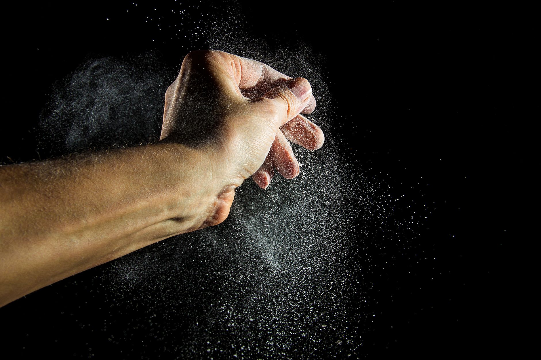 Chalk dust bursts from a lifter's clapped hands against a dark background