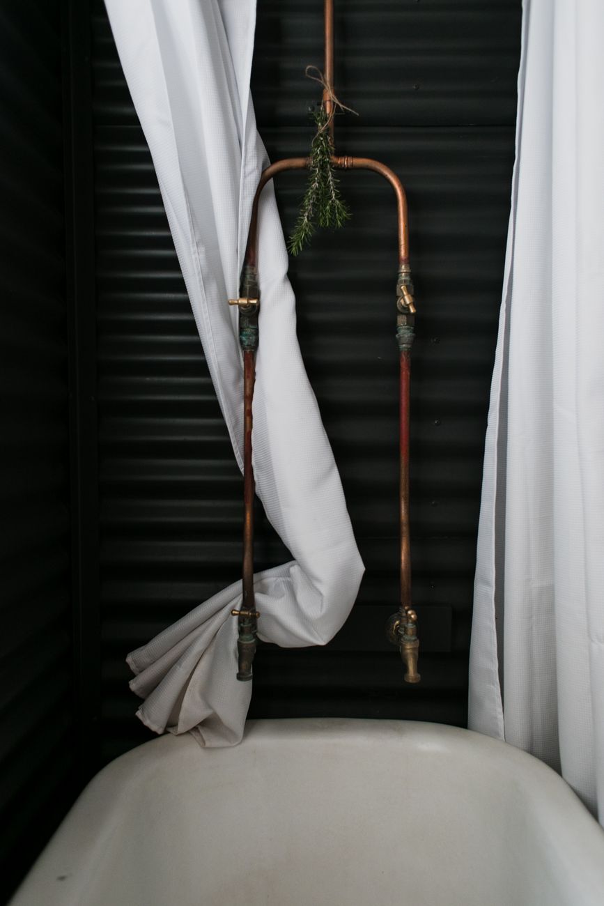 Exposed copper pipes and brass tapware above a clawfoot bath