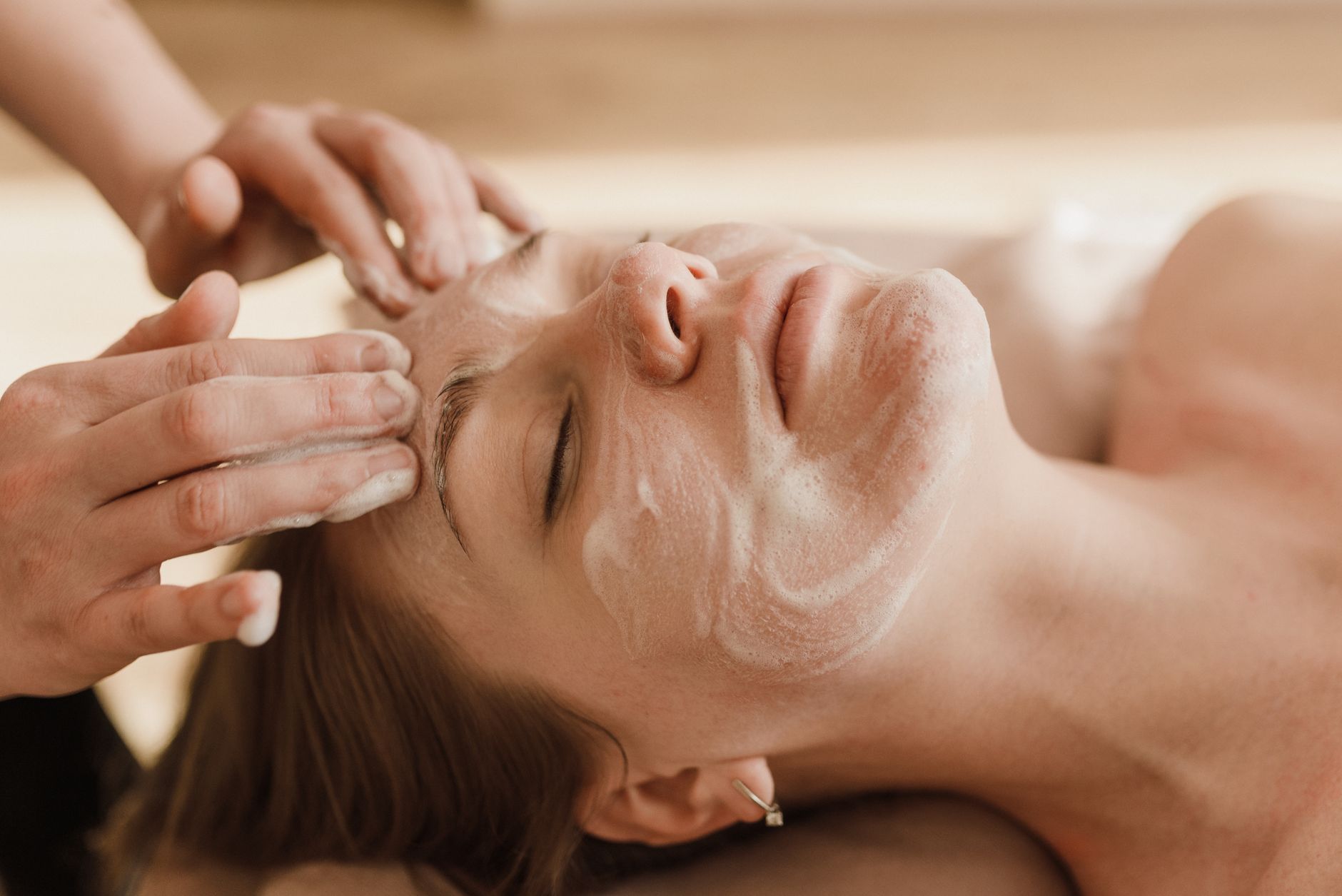 A therapist works a foaming cleanser across a client’s face during a treatment