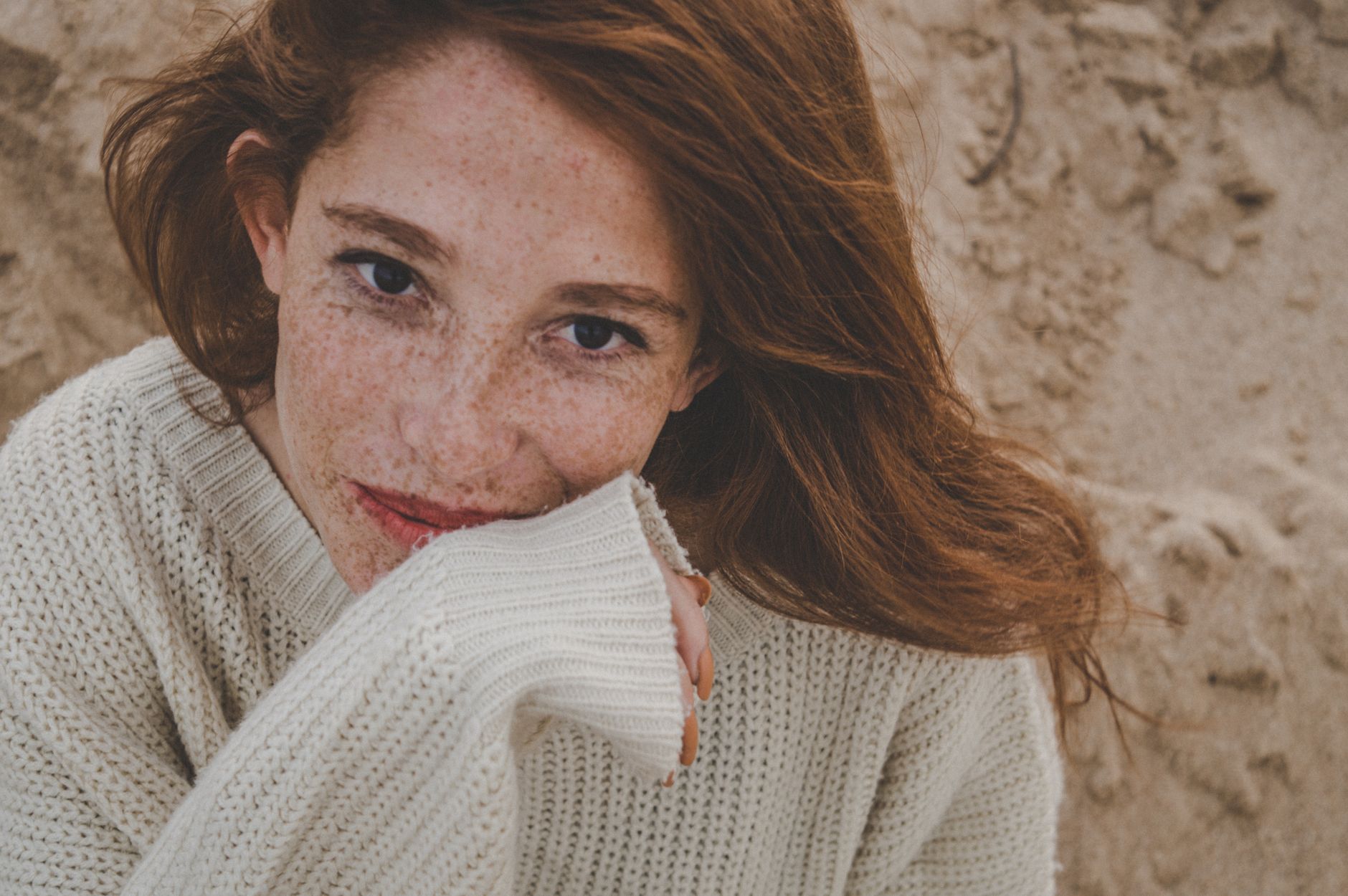 Freya Lindqvist, a smiling woman with freckles, rests her chin on the sleeve of an ivory knit jumper