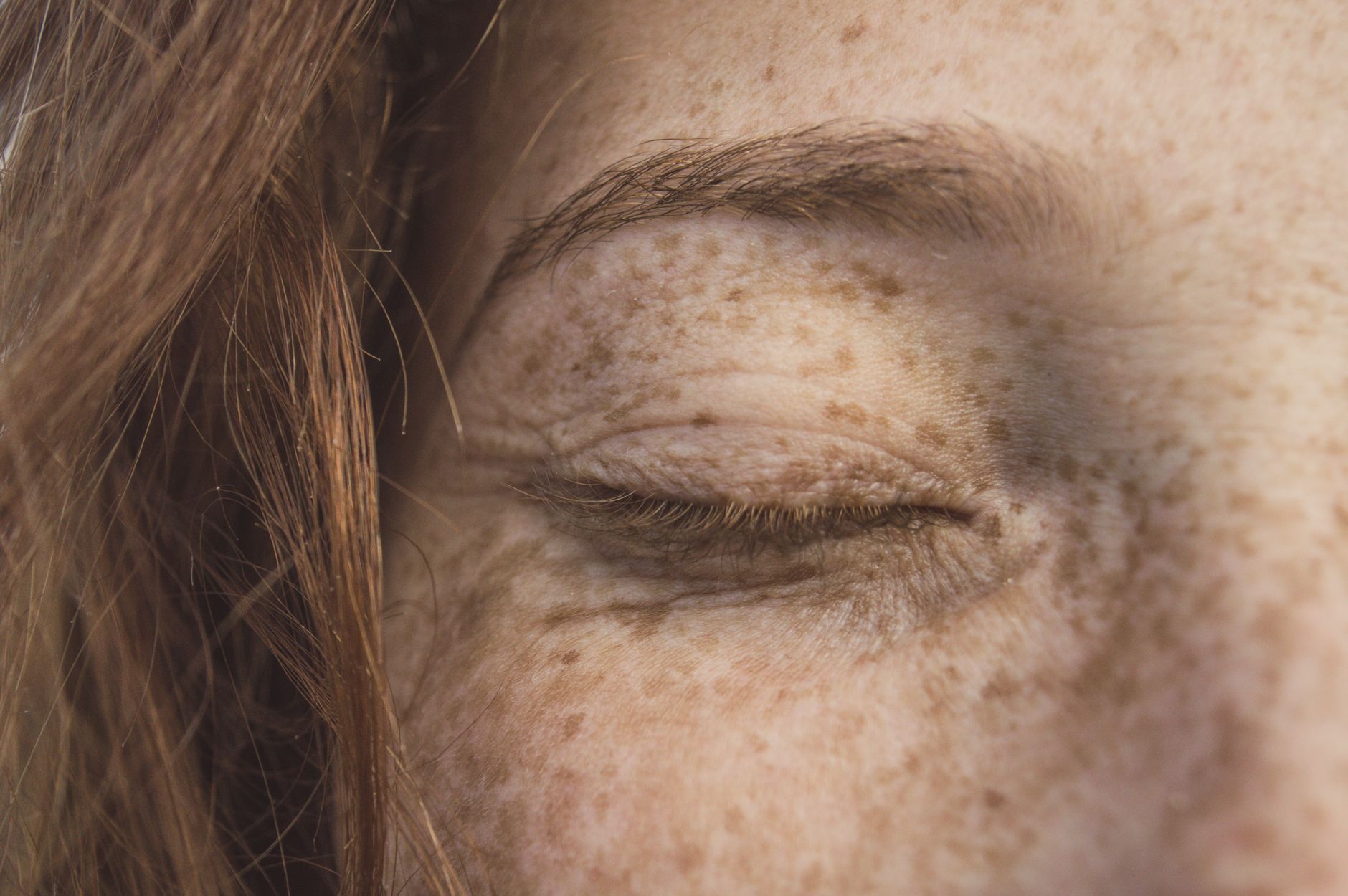 Close view of a closed eye and cheek showing natural freckles and skin texture
