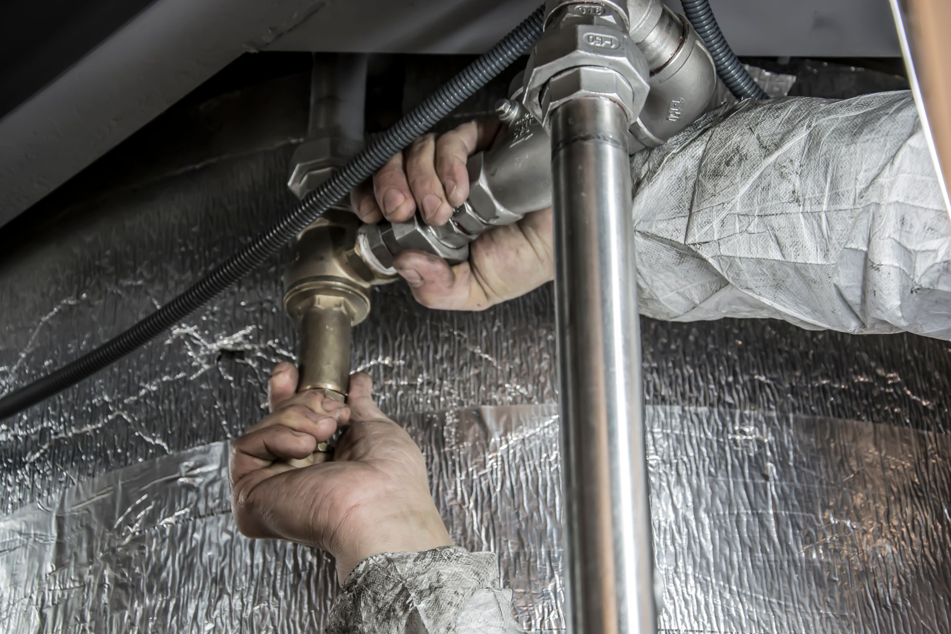 Plumber's hands fitting steel pipe and a brass valve in a tight service space