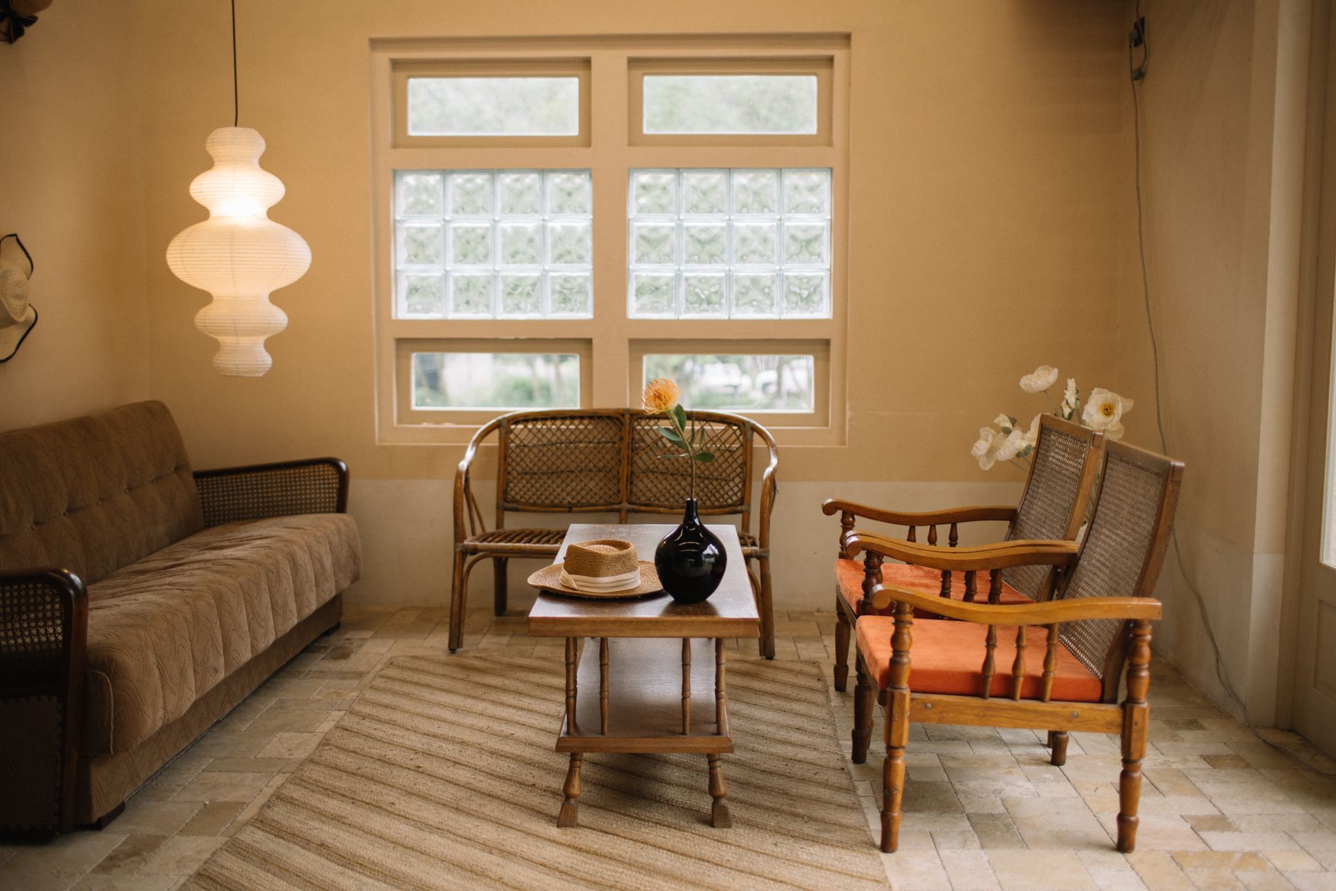 A softly lit sitting room with cane furniture and a paper pendant light in warm neutrals