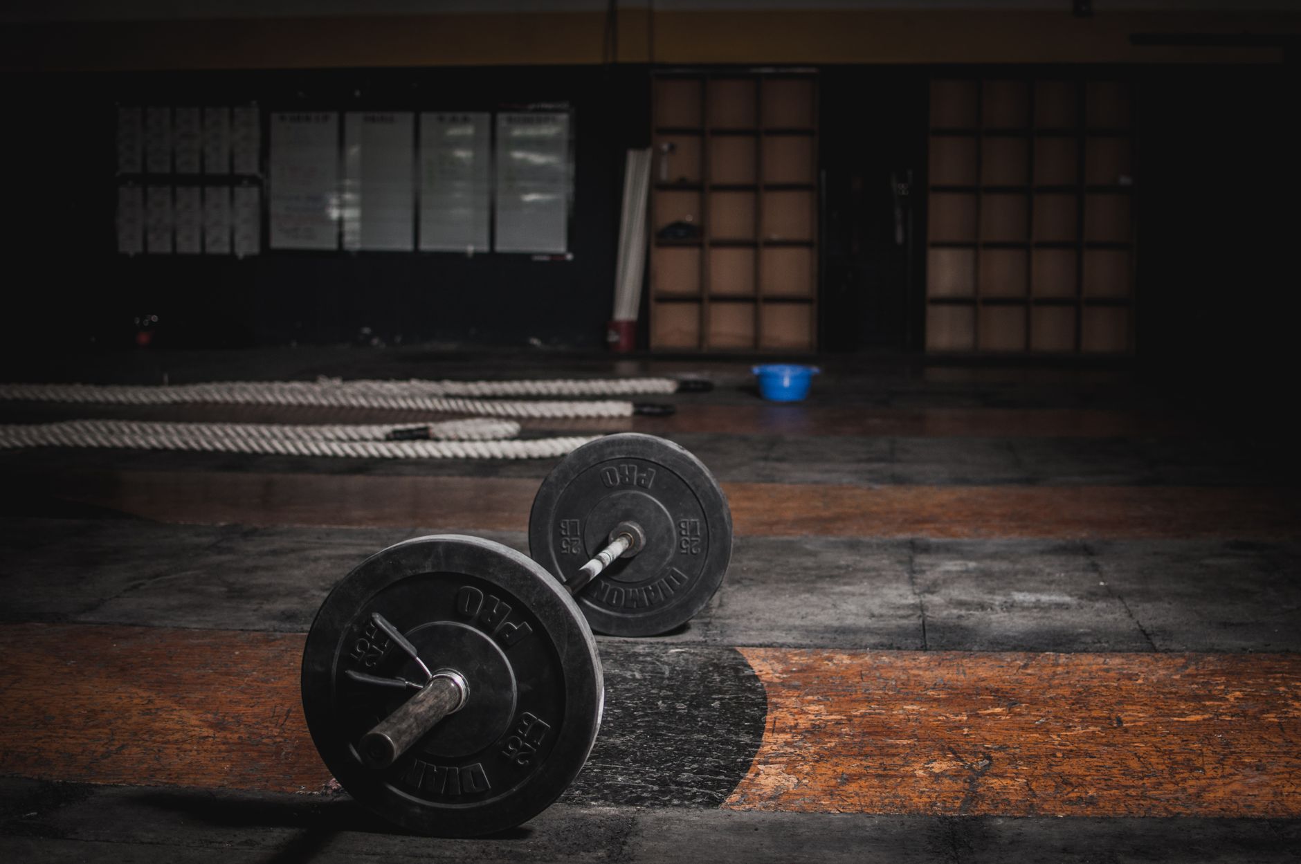 A loaded barbell rests on the worn floor of an empty training gym