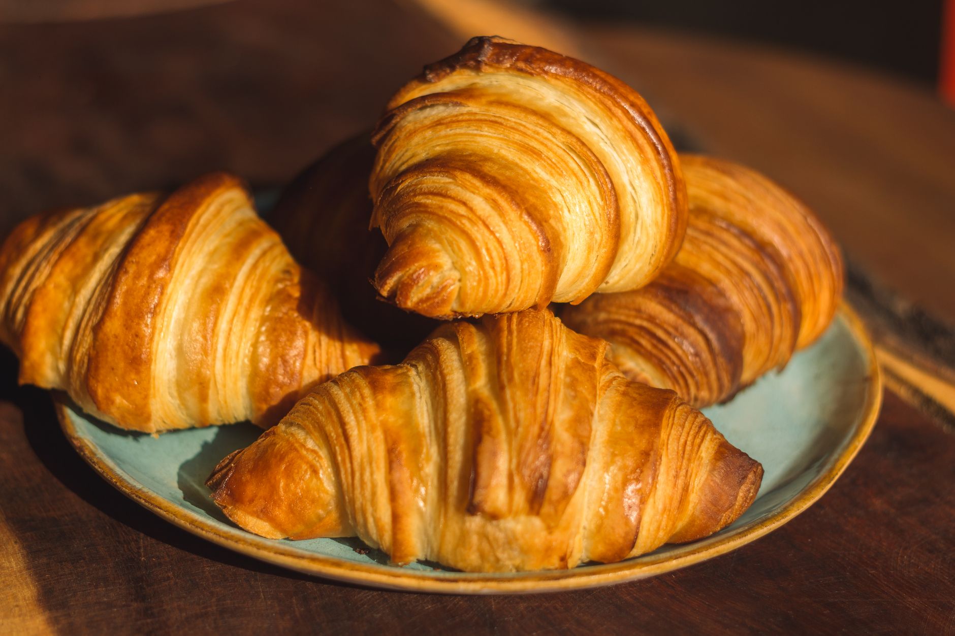 Golden croissants stacked on a plate in warm morning sunlight