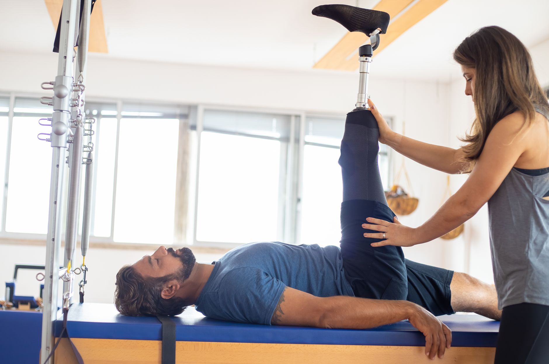 A physiotherapist guides a man with a prosthetic leg through a supported leg raise