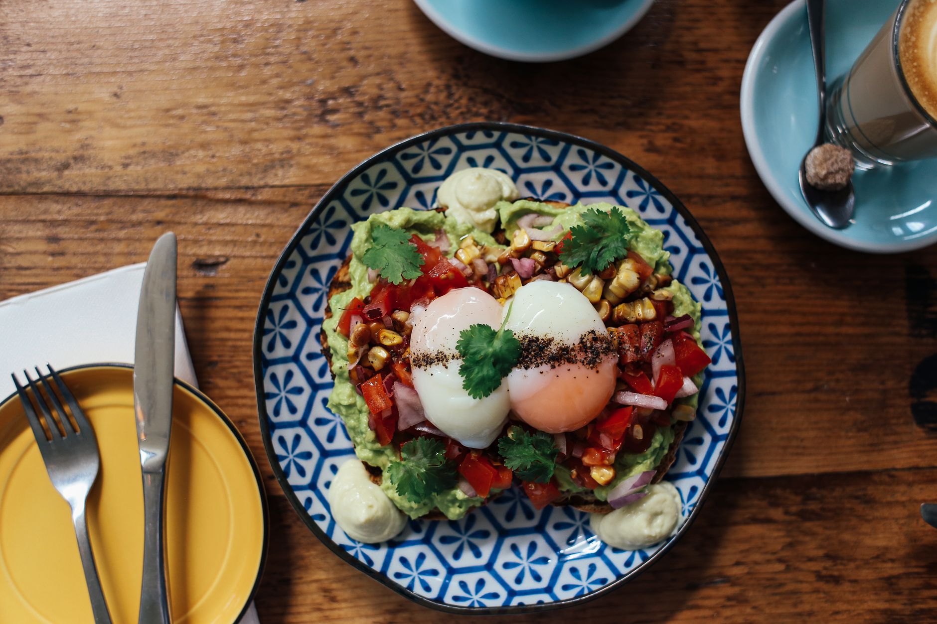 Smashed avocado toast with poached eggs and tomato salsa on a timber table