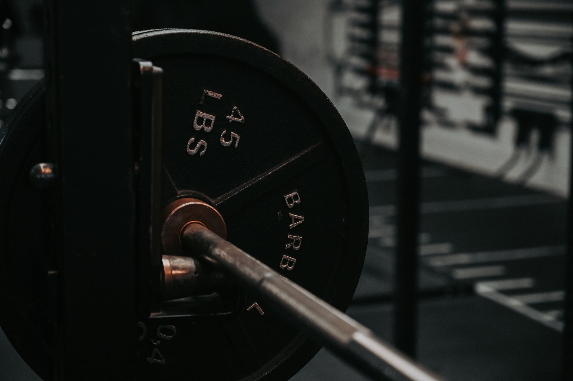 Close-up of a weight plate loaded on a knurled barbell in a dark gym