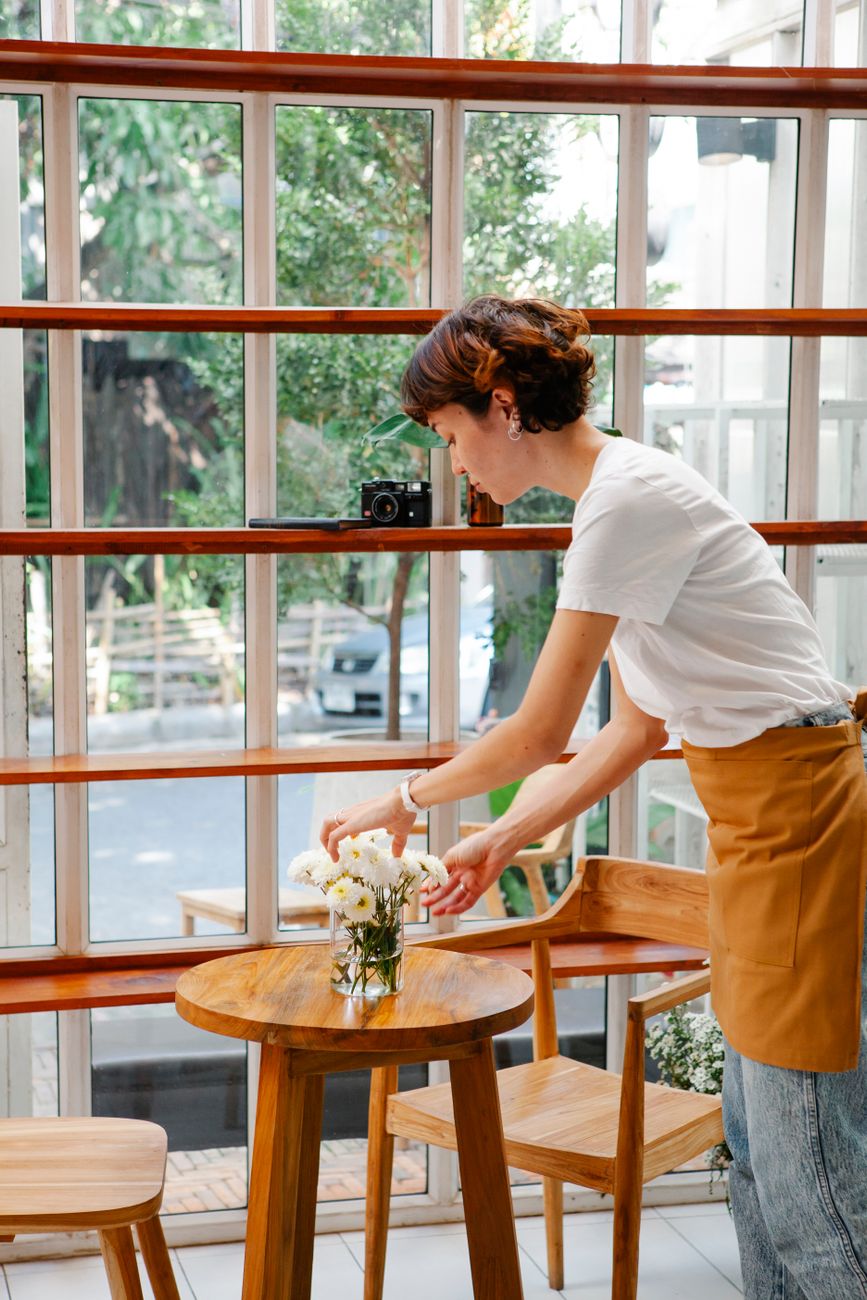 Staff member arranging fresh flowers on a table by the cafe windows