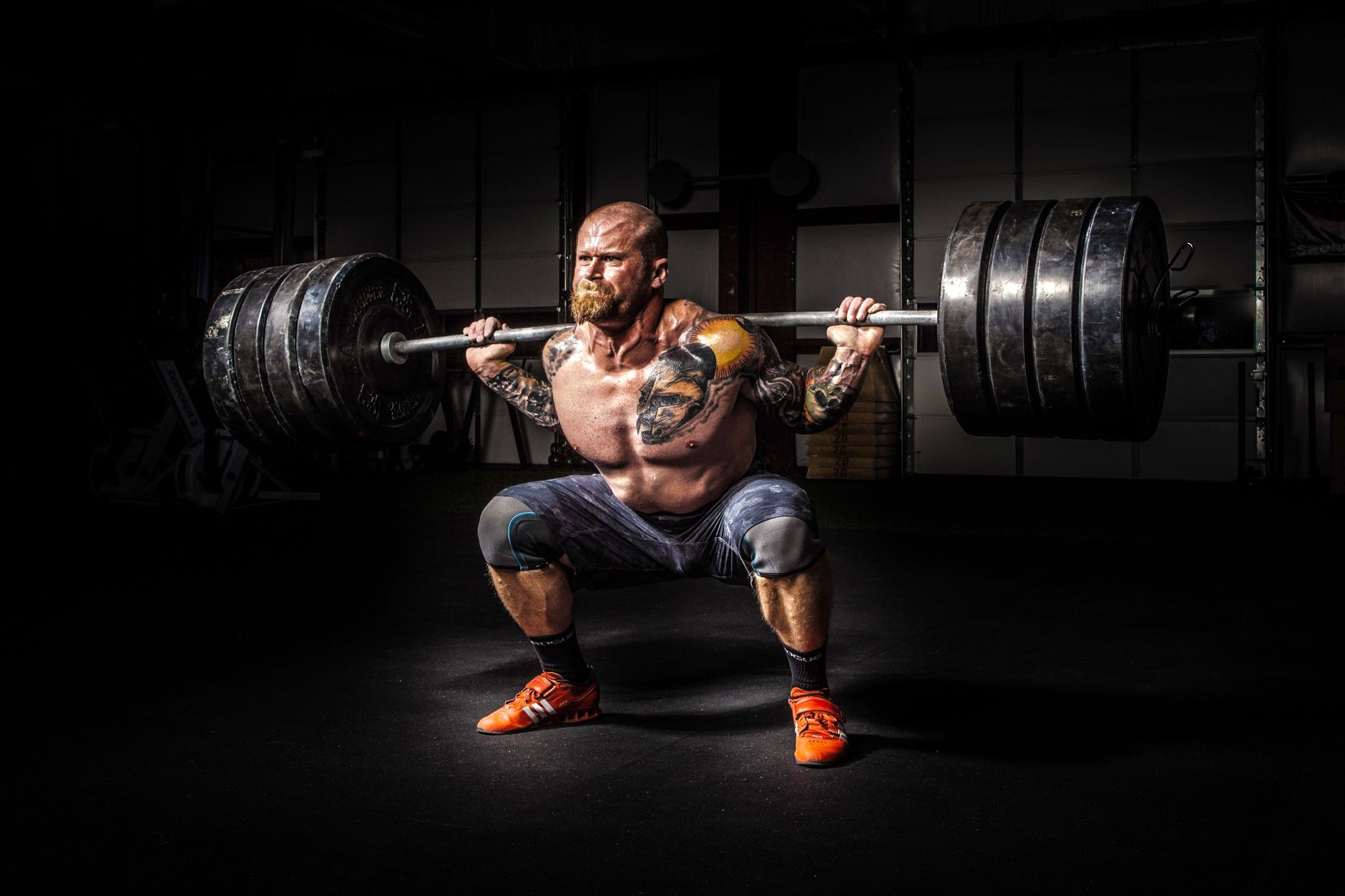 A lifter drives out of the bottom of a heavy barbell squat under a single hard light
