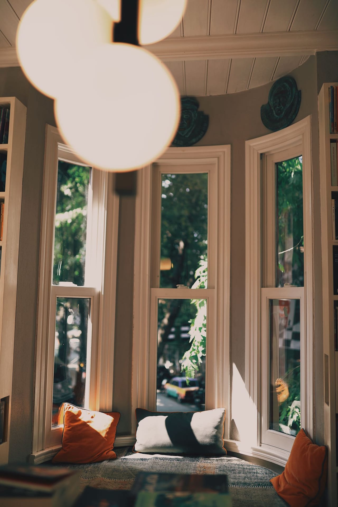 A cushioned bay-window seat with warm cushions and bookshelves, looking onto a leafy street